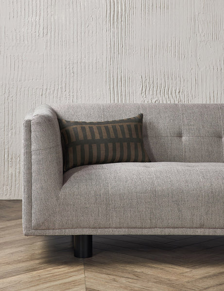 #size::12--x-20- | The Kellan lumbar throw pillow sits on a gray linen sofa in a studio room with hardwood floors