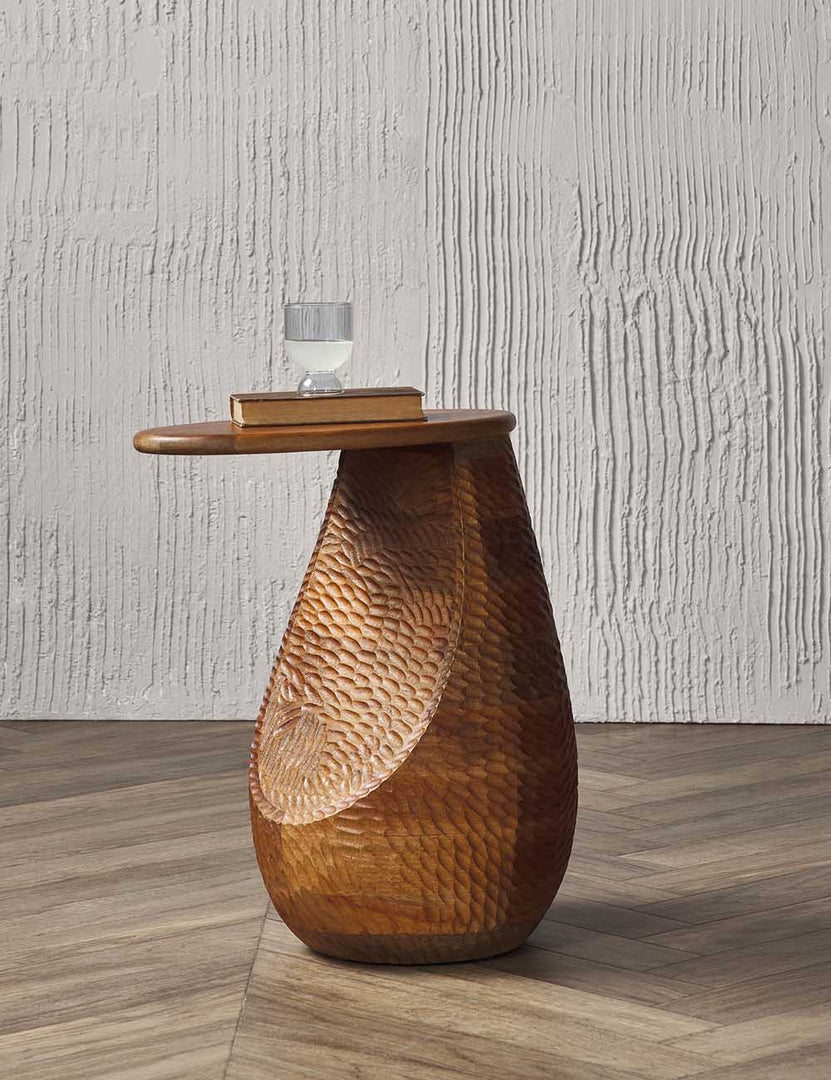 | The Gem mango wood side table sits in a studio with chevron wooden floors and textured walls with a book and glass atop it