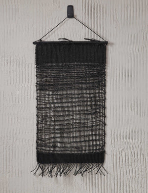 The nyana black wall hanging hangs from an ivory textured wall