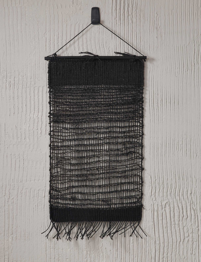 #color::black | The nyana black wall hanging hangs from an ivory textured wall