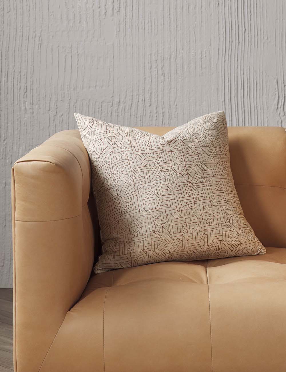 #size::20--x-20- | The Kisha natural-toned square throw pillow sits on a light brown leather button-tufted sofa in a studio room