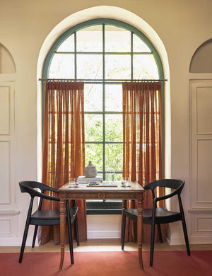 Two Black Ida Dining Arm Chairs sit across from each other with a chess table in between them in front of an arched window