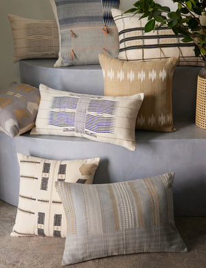 The Imli throw pillow in gray and blue sits on a blue step with other throw pillows