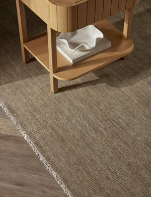 The Heritage moss gray rug lays under a rectangular side table with a book and white ruffle bowl in its shelf