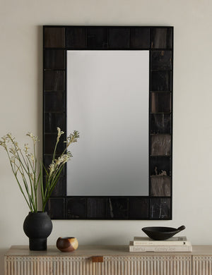 The iron and petrified wood framed Magna wall mirror styled with a black vase and bowl above a console table.