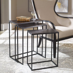 The Loletta black nesting tables are partially nested under each other, sitting in a living room next to a black wooden framed accent chair atop a gray patterned rug