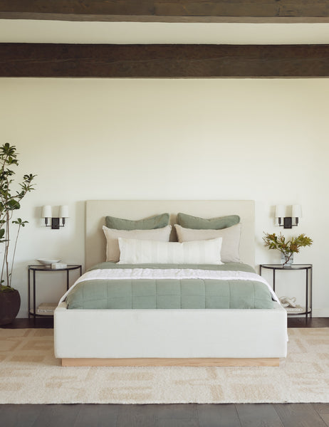 #color::natural #size::cal-king #size::king #size::queen  | The Lockwood natural velvet-upholstered bed with a white oak base sits in a neutral bedroom with a plush natural rug and wooden ceiling beams. 