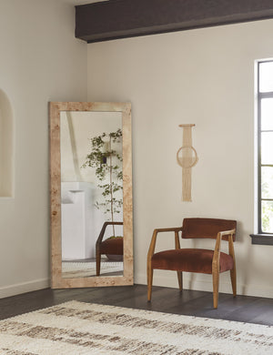Bree Burl Wood Rectangular Floor Mirror sits in the corner of a room with a cognac velvet accent chair and a natural wall hanging