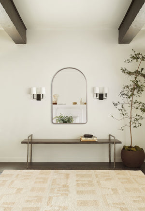The Shashenka arched wall mirror with silver frame hangs in a room with beamed ceilings above a metal bench