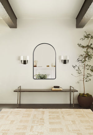 The Shashenka arched wall mirror with black frame hangs in a room with beamed ceilings above a metal bench