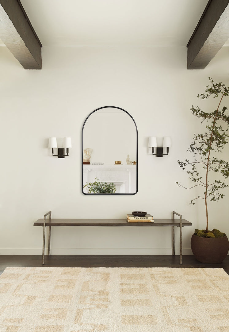 #color::black #size::38--x-24- | The Shashenka arched wall mirror with black frame hangs in a room with beamed ceilings above a metal bench