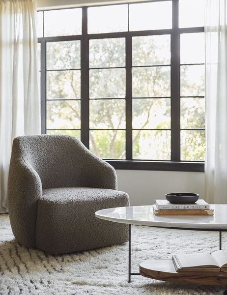 #color::gray-boucle | The Tobi gray boucle swivel chair sits atop a plush ivory rug in front of a wall with large black-framed windows and sheet curtains