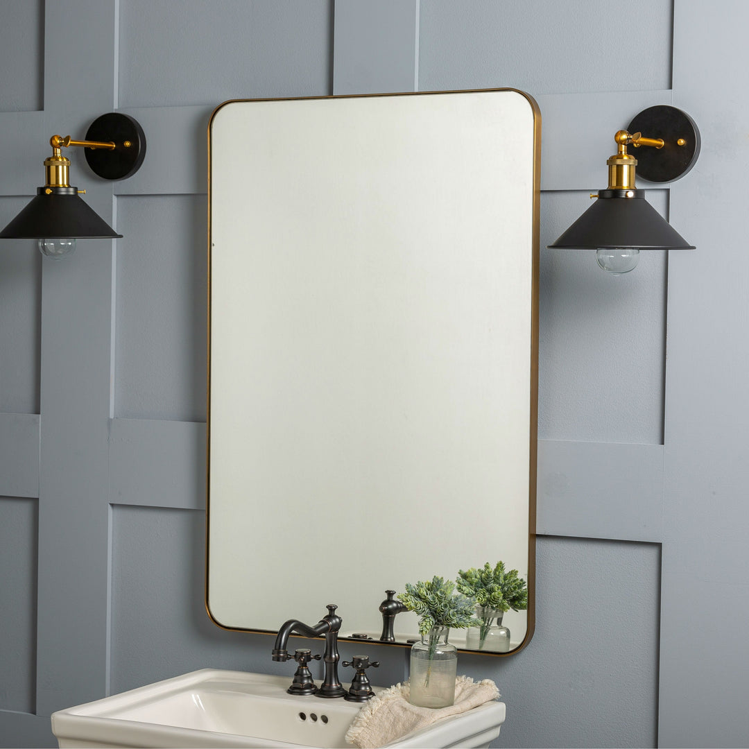 #color::gold #size::36--x-24- | The Lyta rectangular golden framed wall mirror with rounded corners hangs on a blue accented wall in between two black sconce lights