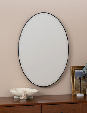 Luke black oval mirror hangs above a wooden sideboard on a beige-toned wall