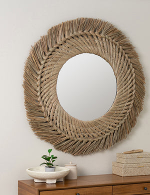 angled view of the Sunniva round woven seagrass decorative mirror hanging on the wall above a console table