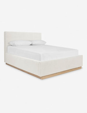 An angled side view of the Lockwood white velvet-upholstered bed with a white oak base.