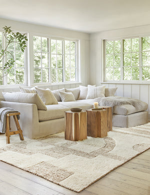 The Oasis plush geometric neutral-toned rug by Élan Byrd lays in a bright living room with a gray linen sofa, t-shaped wooden side tables, and neutral-toned throw pillows