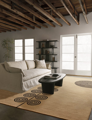 The Laci natural rug lays in a living room with wooden beamed ceilings under a black coffee table and slipcover sofa
