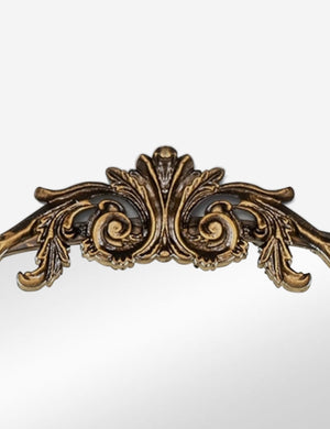 Detailed view of the traditional scroll detailing on the top of the Tulca gold curved standing mirror with flat bottom edge.
