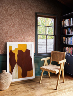 The Alaari Wallpaper is in a room with a black bookshelf, a woven chair, a jute basket, and a warm-toned wall art