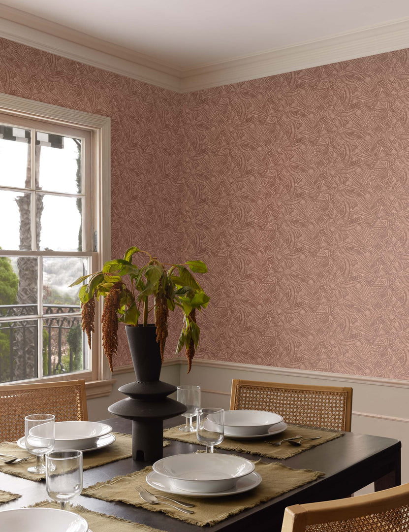 | The Alaari wallpaper is in a dining room with a black dining table, rattan dining chairs, and white serveware
