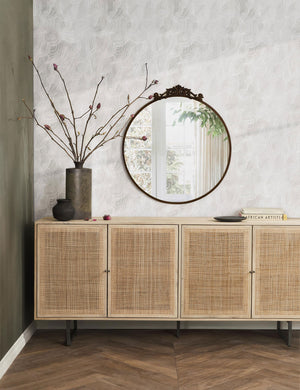 The tulca oil rubbed bronze round mirror hands on a wall above a rattan sideboard next to a brown vase