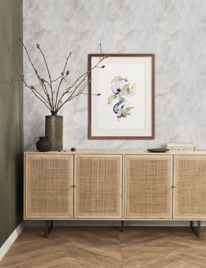 The Awakening Spring Print in a walnut frame hangs above a rattan sideboard on a chevron wooden floor