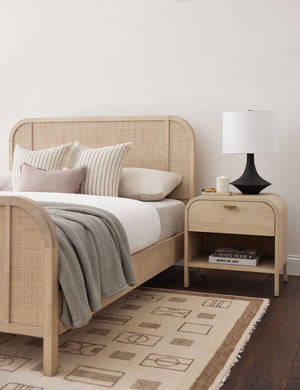 The Coulwood black table lamp with sculptural base sits in a bedroom with light wood and woven framed bed, a light wooden nightstand, and a natural toned patterned rug