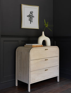 The Ride Print in a golden frame is hung on a black wall above a white washed three drawer dresser