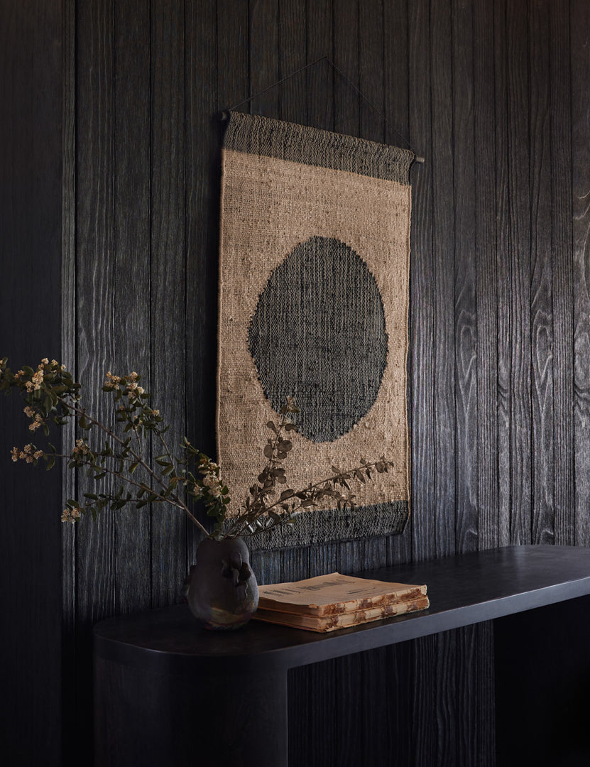 | Katlee black and natural flat weave Wall Hanging with circle in the center hangs on a black wooden wall above a black console table
