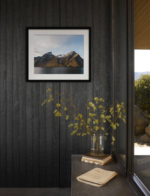 The Fjords Photography Print hangs on a black wood paneled wall next to floor to ceiling windows and a clear vase