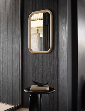 The Bourdon natural Mirror hangs on a black wood paneled wall above a black wooden round side table