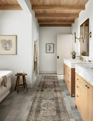 Billie Rug in clay and sage by Amber Lewis x Loloi in its runner size lays in a bathroom with his and hers sinks and a white bathtub