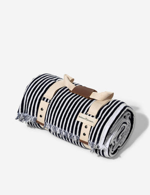 The Navy and white striped cotton beach blanket by business and pleasure co wrapped up in the leather-handled strap