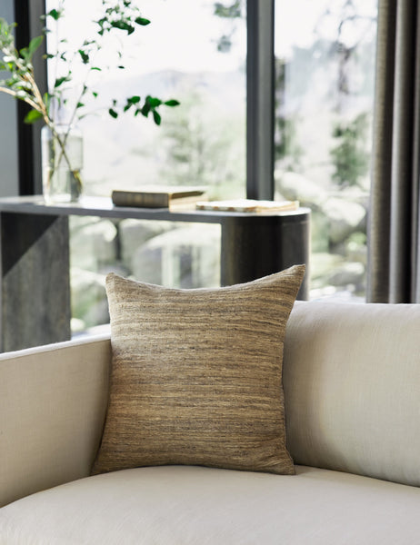 | The Bryce natural-toned silk square pillow sits natural linen sofa in a room with floor to ceiling windows