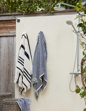 Navy and white striped Beach Towel by Business & Pleasure Co hangs from an outdoor shower space with another towel