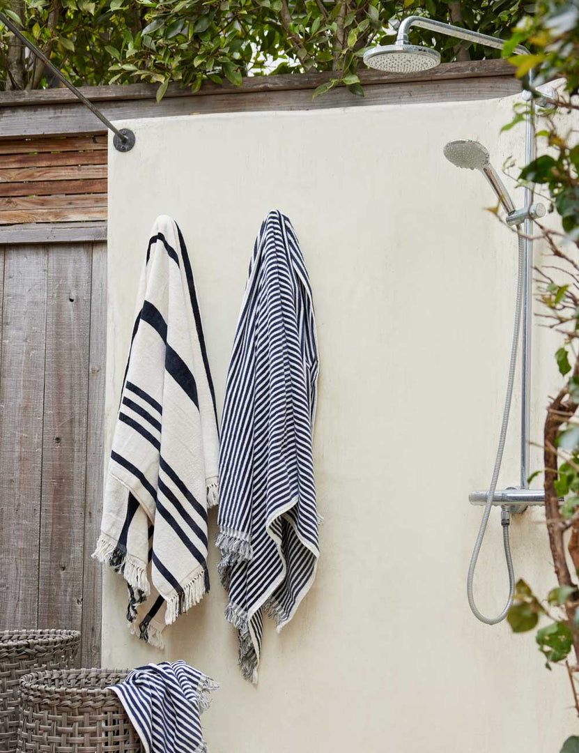 #color::navy-stripe #style::navy-stripe | Navy and white striped Beach Towel by Business & Pleasure Co hangs from an outdoor shower space with another towel