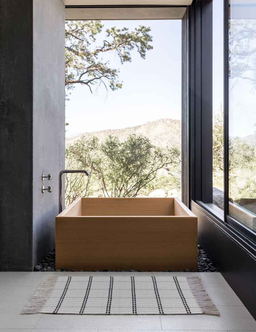 #size::1-9--x-2-10- #size::2--x-5- | Elin mat lays on a tile floor in a bathroom with a rectangular wooden bath, black walls, and floor to ceiling windows