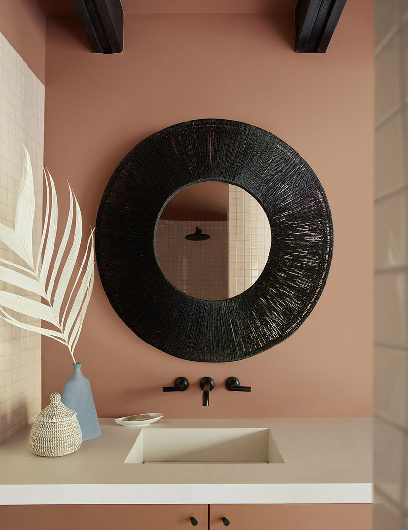 | The Carlotta Round Mirror hangs in a bathroom against a terracotta wall above a white sink with black hardware
