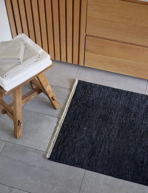 The Heritage indigo runner rug lays in a bathroom on a gray tiled floor next to a stool with bath linens