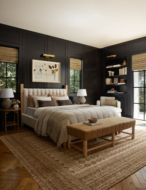 The Ambleside natural linen bed sits atop a patterned rug in a room with accented black wooden walls and a orange linen bench