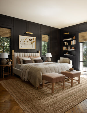 The Keziah moss rug lays in a bedroom with black walls under an upholstered bed with two upholstered ottomans
