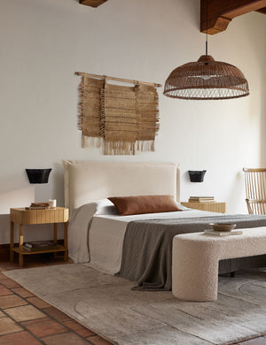 The arlo Burnt Orange long lumbar pillow sits on a natural linen framed bed below a jute chandelier and wall hanging