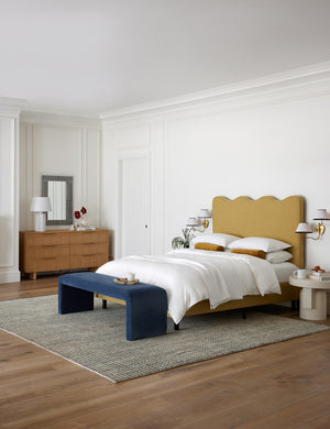 Clementine golden linen platform bed with undulating lined headboard sits in a bedroom with a blue velvet bench and a black and white area rug