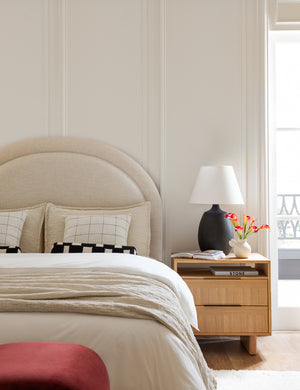 The Odele talc linen platform bed has beige linens and throw pillows laying atop it next to a 2-drawer nightstand