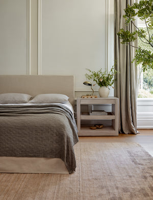 The Ojaj pebble cotton matelassé coverlet by pom pom at home lays atop a gray linen framed bed in a bedroom with a gray plush rug and a white washed wooden nightstand