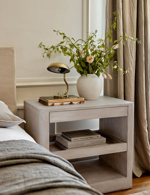 The Arabel light wood open nightstand with two pull-out drawers has a brown vase with dried botanicals and a stack of books.