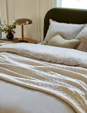 The Ojaj greige cotton matelassé coverlet by pom pom at home lays on an emerald framed bed with a gray duvet and pillow