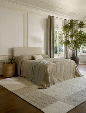 The Woburn Rug lays in an ivory bedroom with tall windows under a neutral linen framed bed