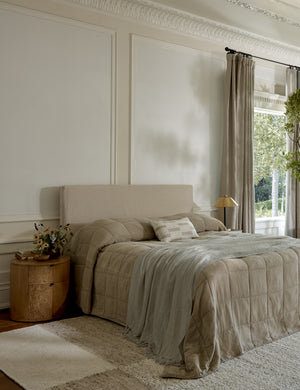 The Montauk natural linen blanket with tasseled ends by pom pom at home lays at the edge of a natural linen framed bed in a bedroom with accented walls and a plush rug